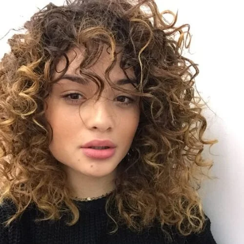 Natural curly hairstyle featuring soft textured bangs that beautifully frame the face with organic curl definition
