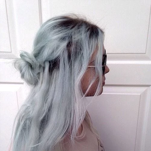 Faded icy blue hair with visible roots styled in half-up messy bun