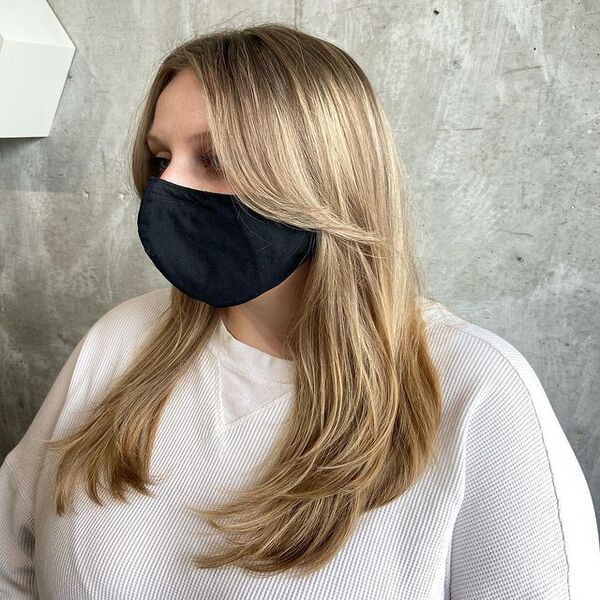 Buttery Blonde Highlights for Long Length Layered Hair - A woman wearing a black mask