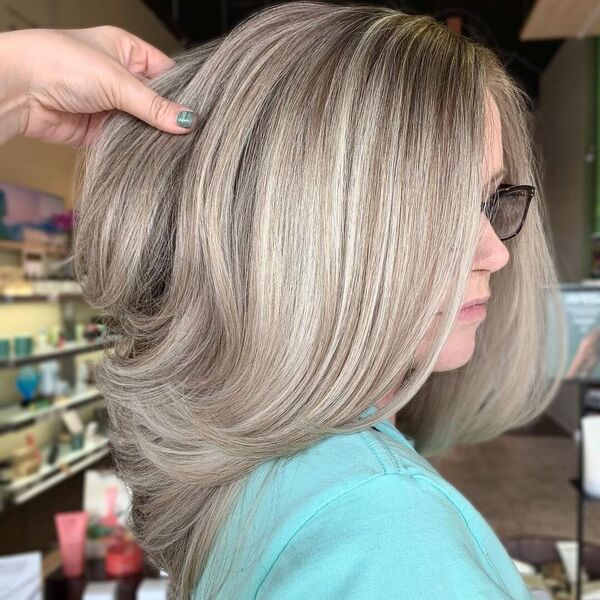 Bouncy Layered Ash Blonde Highlights - a woman wearing glasses in sky blue shirt.