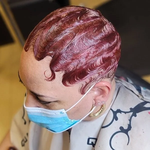 Burgundy Stiff Finger Waves - a woman wearing mask in multiple earrings in salon cape.