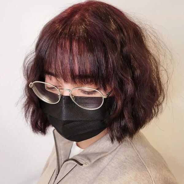 Chin Length Burgundy with Bangs - a woman wearing mask and glasses in beige sweater.