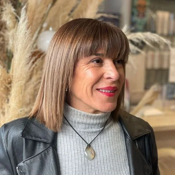 Straight Hair with Blunt Bangs - a woman wearing black leather jacket over gray knitted top.