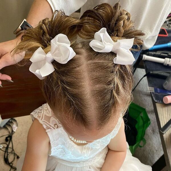 Two Messy Bun Braids Flower Girl Hairstyles- a girl is wearing white dress with pearl necklace.