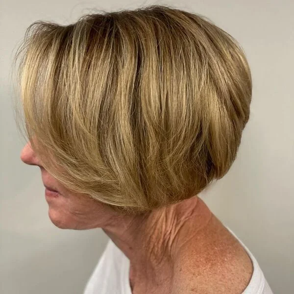 Classic stacked bob with volume, side-swept curtain bangs and golden blonde color - age-defying short sassy haircut for warm undertones